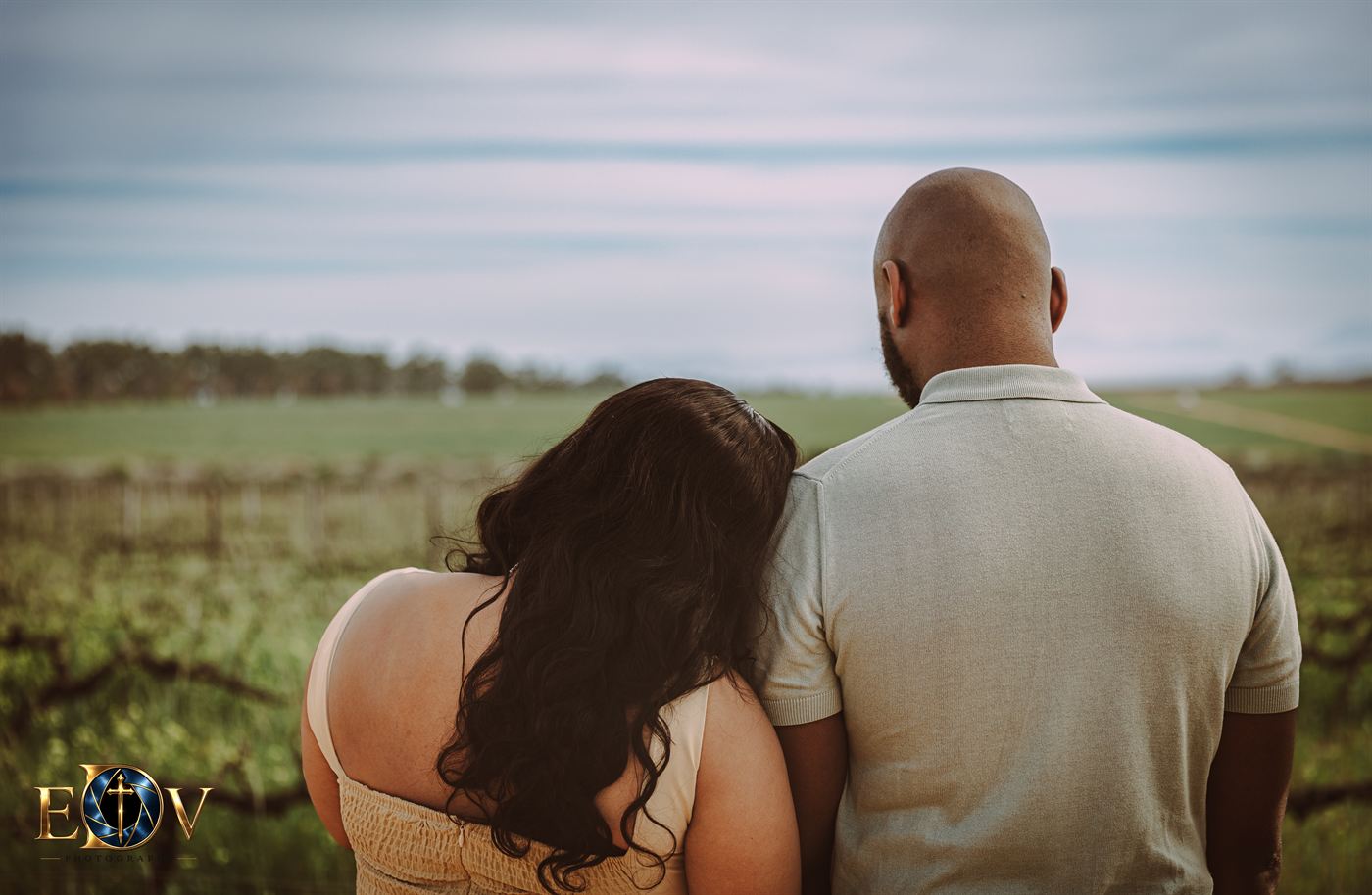 Couple photographed from behind looking out over a vineyard at dusk