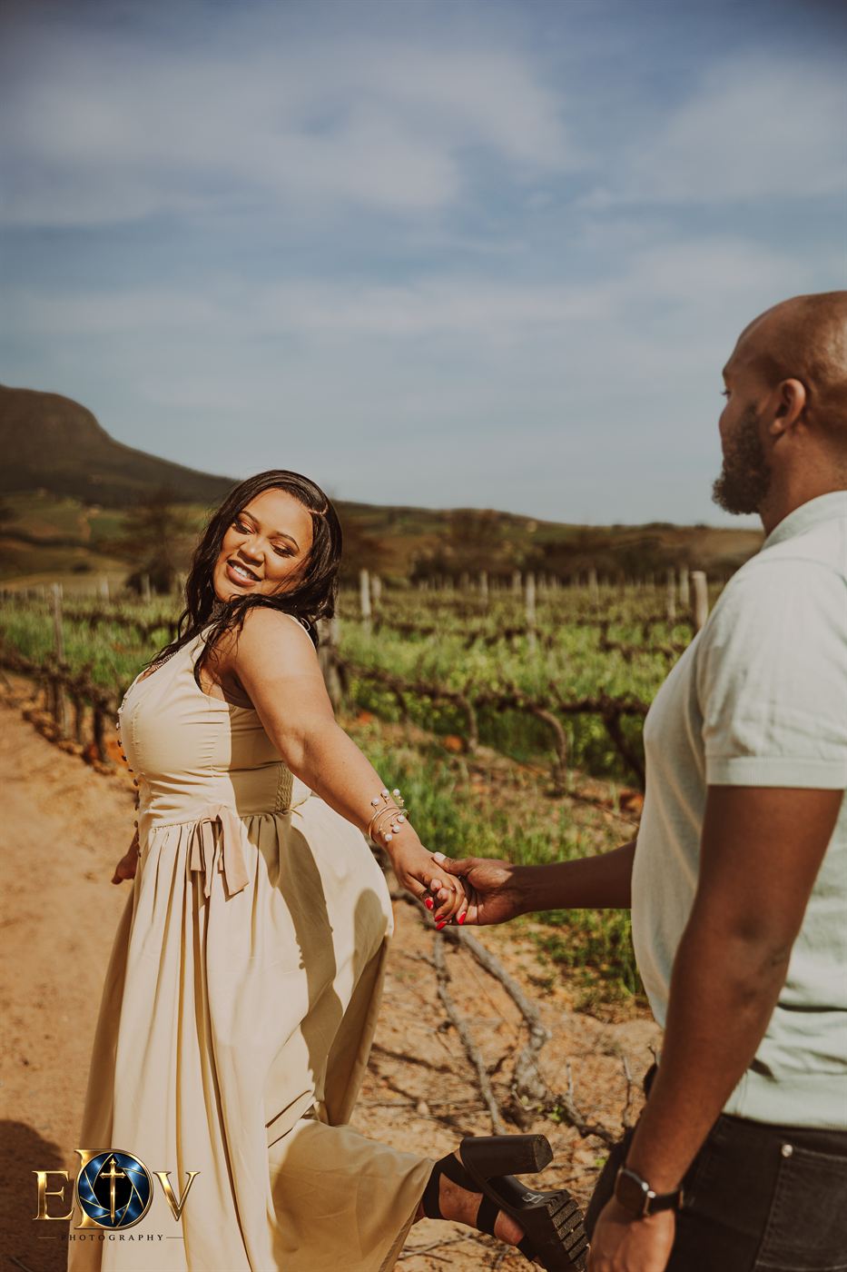 Woman leading her partner by the hand down a row of vines