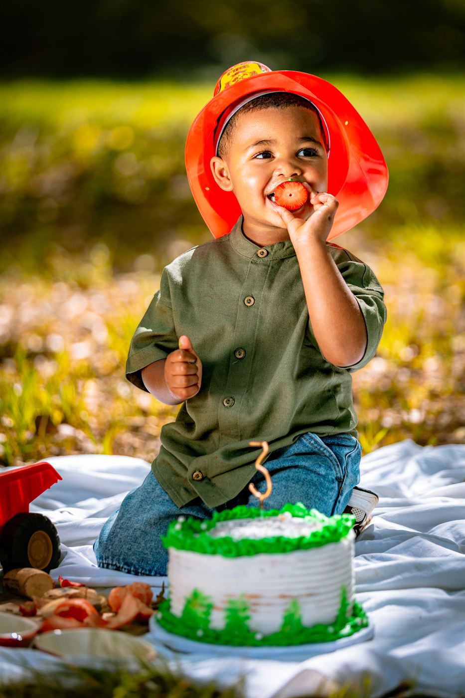 Small boy in a toy fire helmet beside his third birthday cake