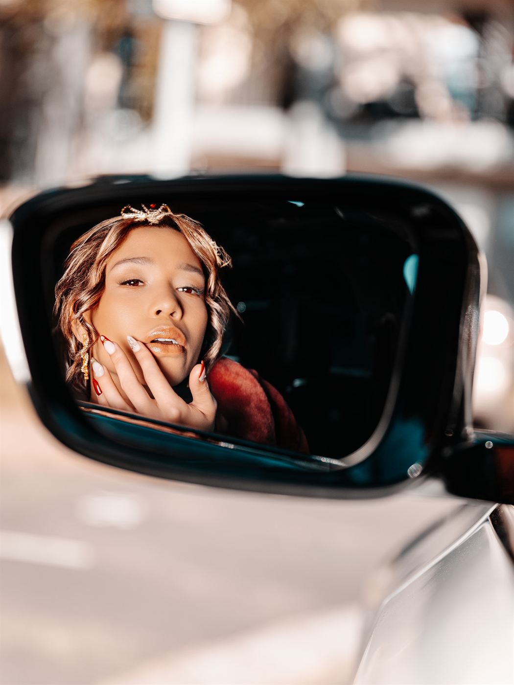 Young woman reflected in a car wing mirror, hand resting at her chin