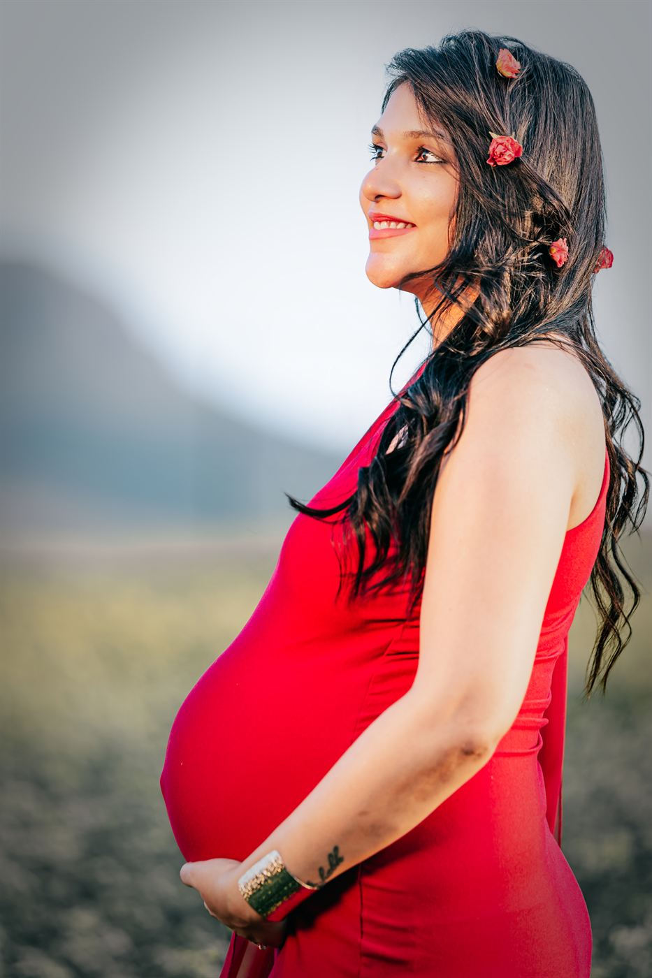 Expectant mother in a red gown photographed in profile against the mountains