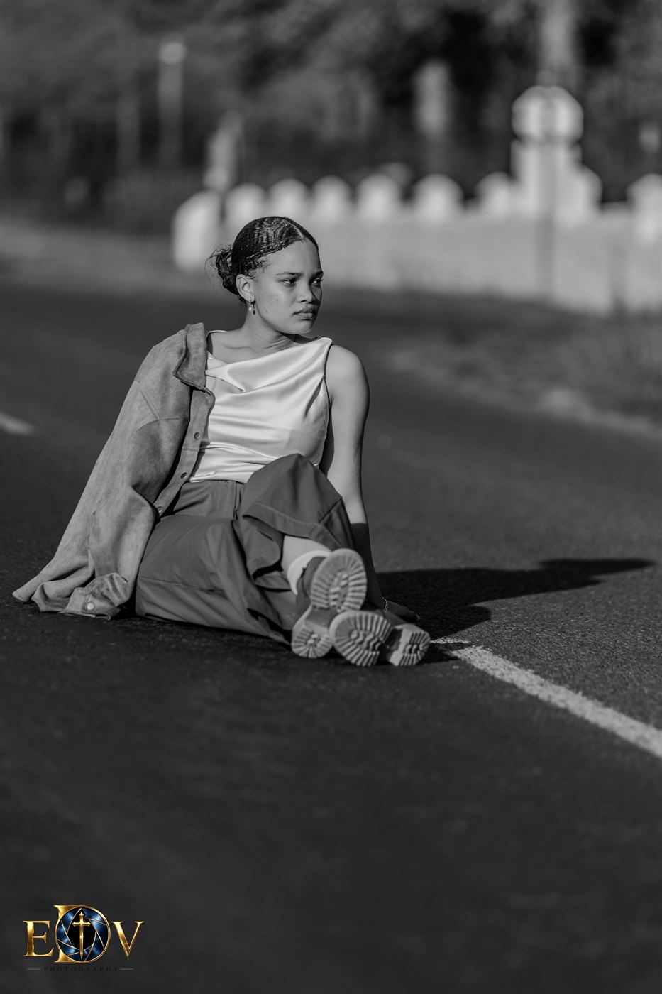 Black and white portrait of a young woman seated on a quiet road