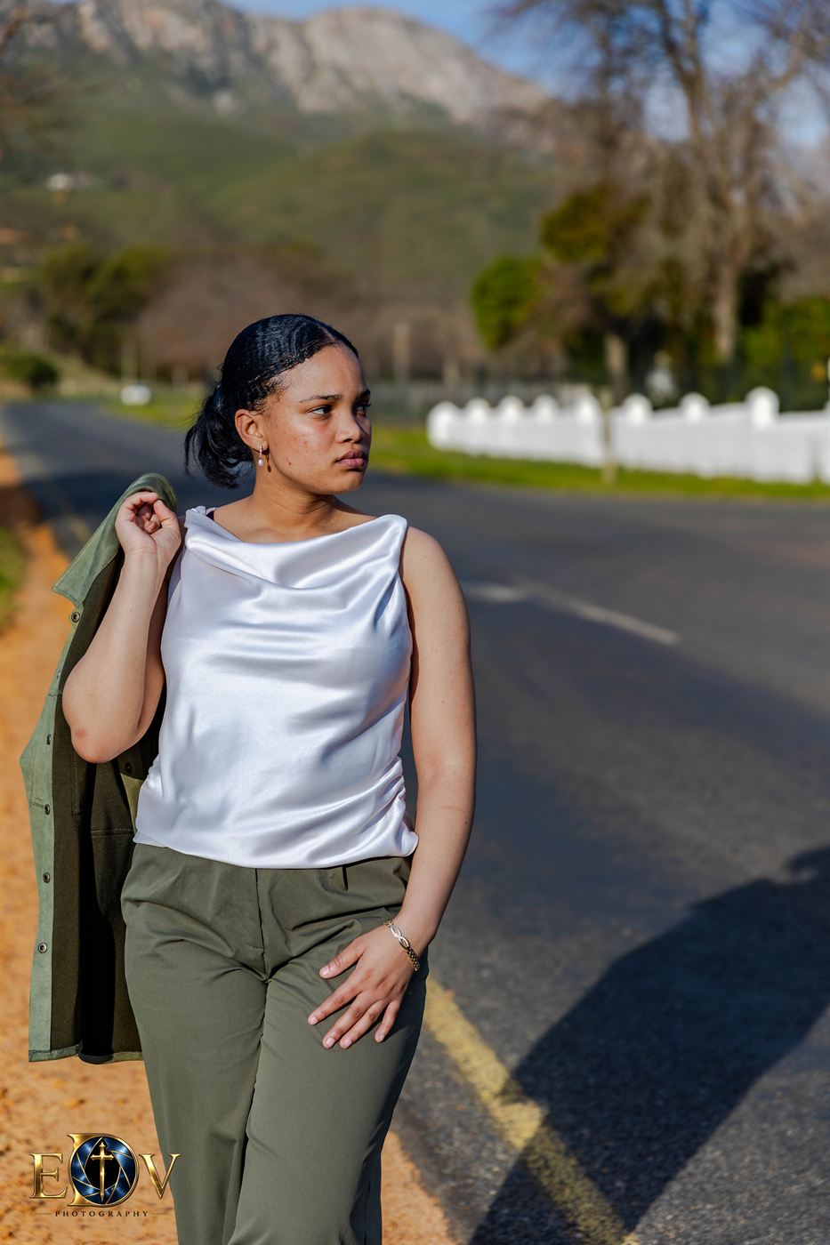 Outdoor portrait session — young woman walking a mountain road with a jacket over her shoulder