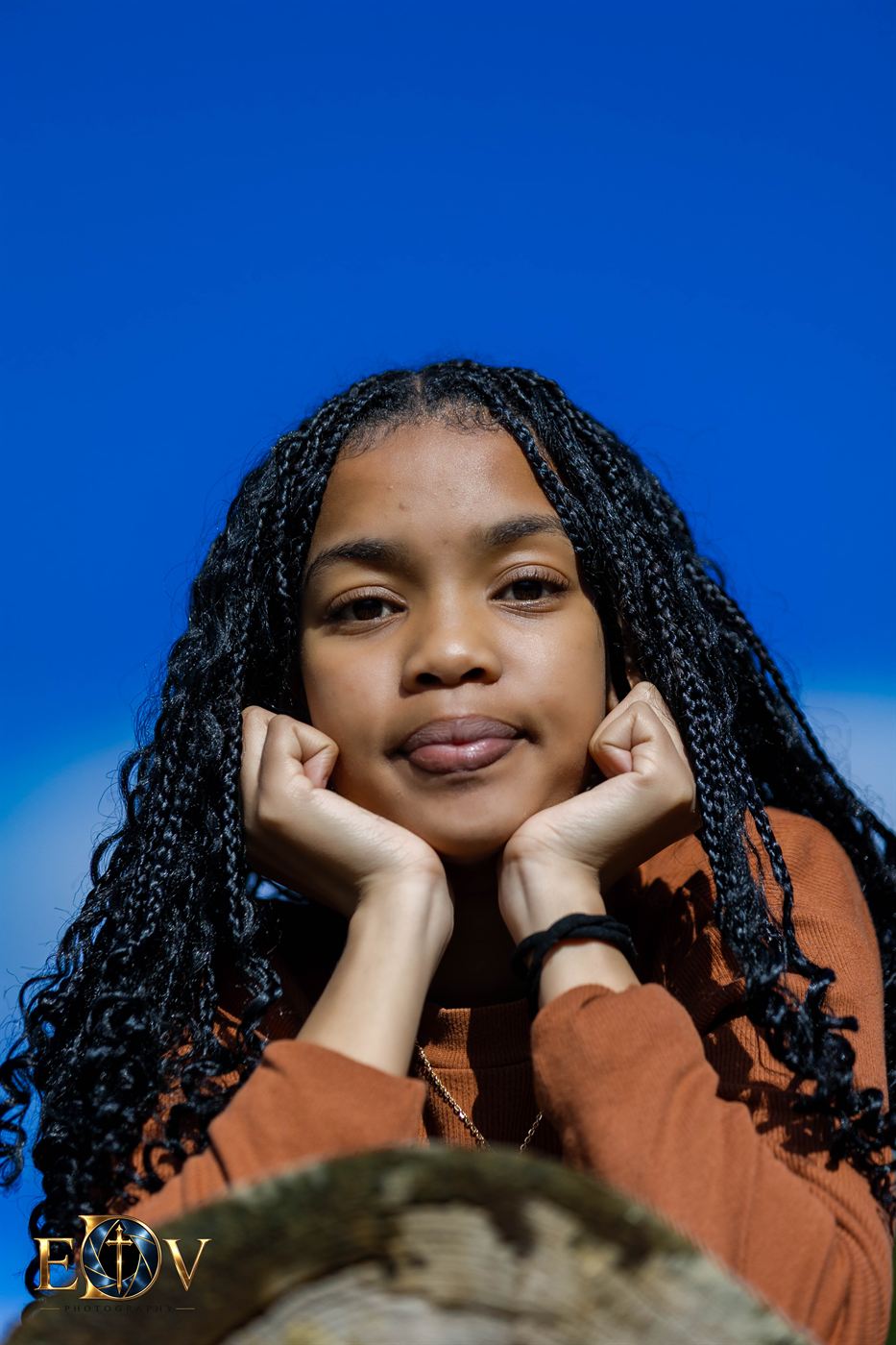 Young woman resting her chin on her hands against a deep blue sky