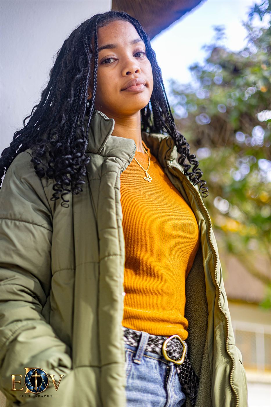 Young woman in a green winter coat photographed against a whitewashed wall