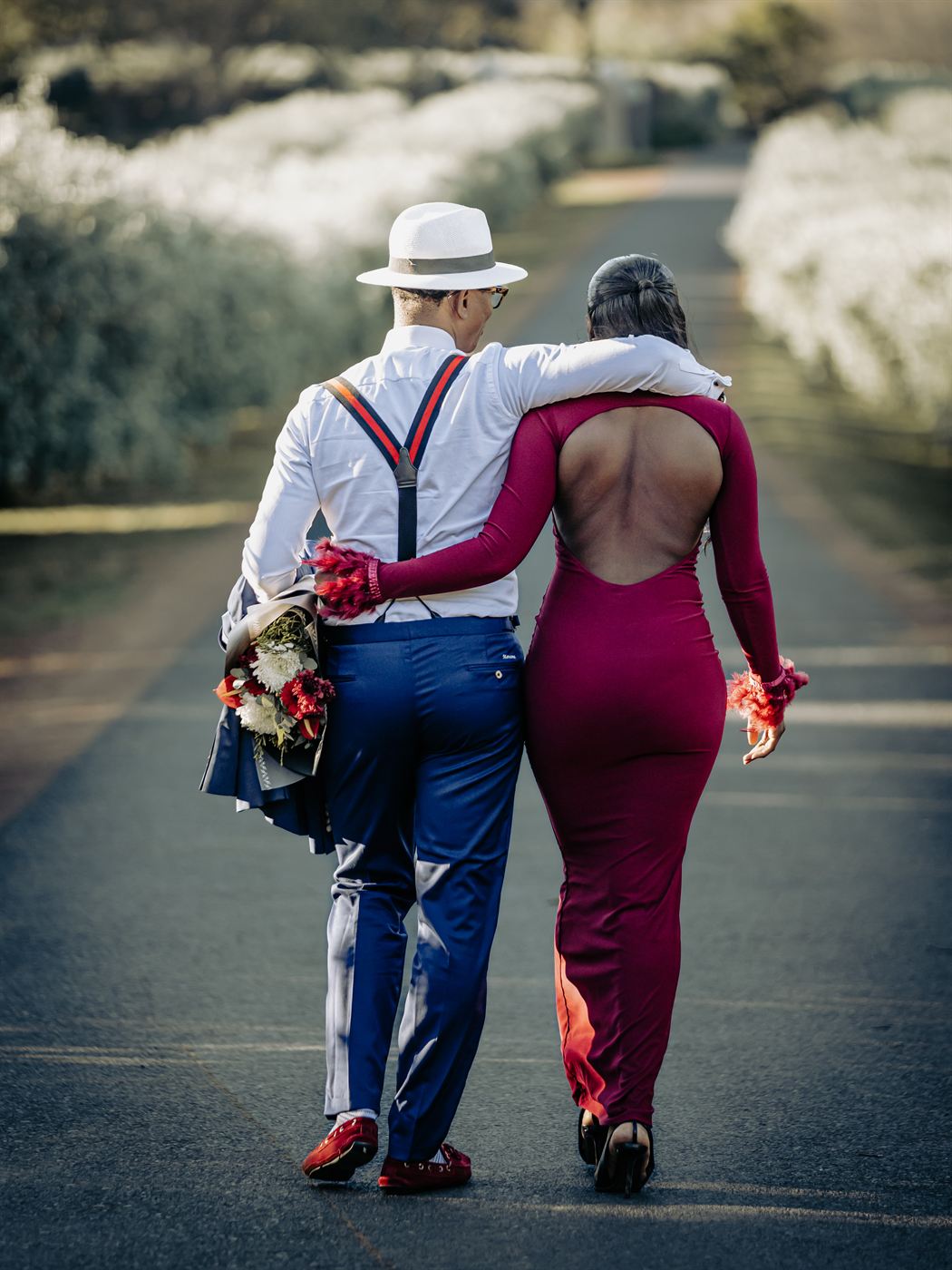 Couple walking away down an avenue of white blossom, she in an open-backed red gown