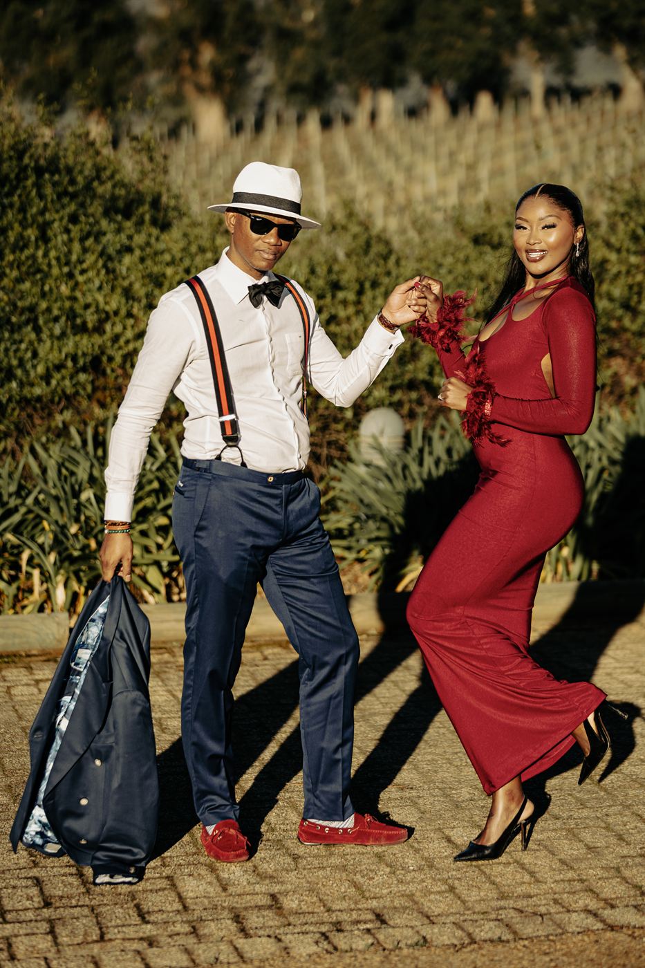 Couple mid-dance on a sunlit path, long shadows across the paving, she in red
