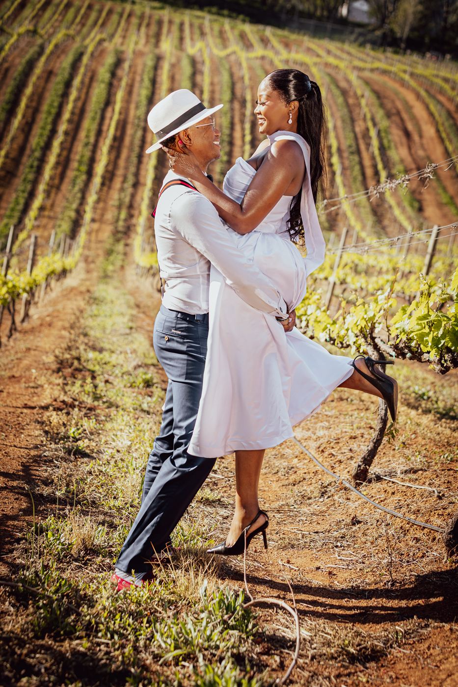 Groom sweeping the bride off her feet between rows of vines, her dress flying